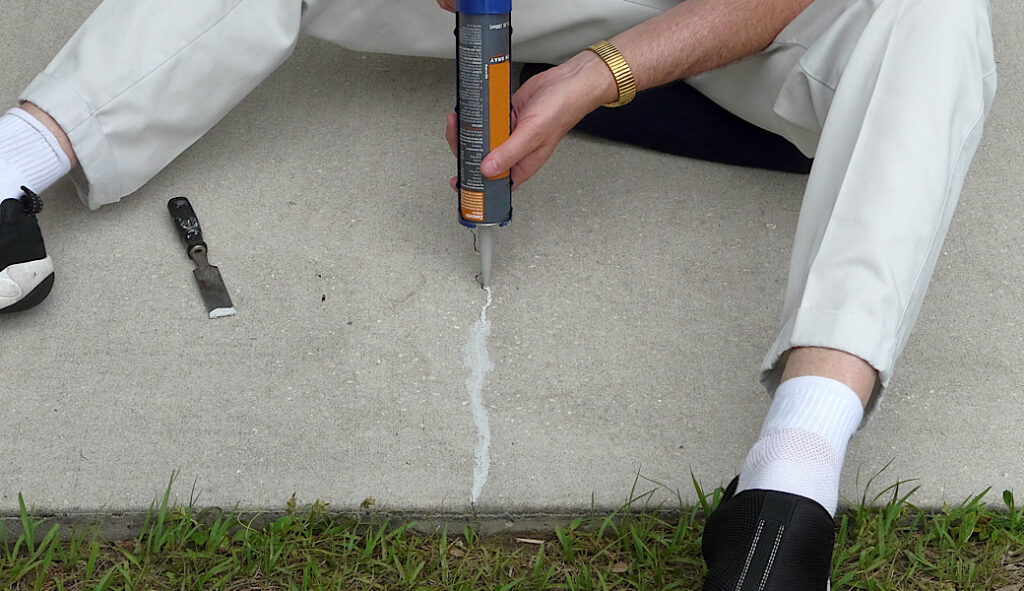 Man filling a crack in patio block with a caulking gun and putty knife